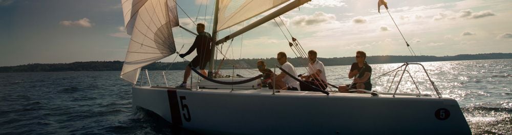 Група хора се наслаждават на ветроходство с платноходна лодка в открито море по залез.