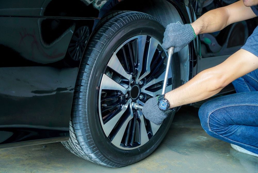 Мъж със сиви ръкавици използва инструмент за смяна на гума на автомобил — поддръжка за колата.